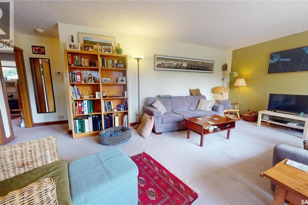 Living room with beige carpet, blue sofas, wood bookshelves, and a red oriental rug. - 203 Pottery Street, Eastend