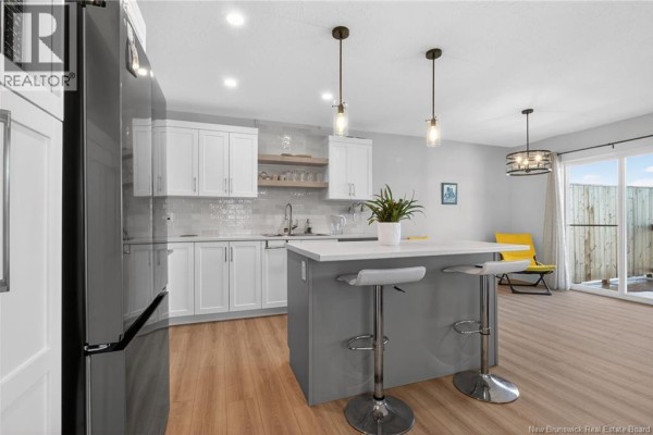 Modern kitchen with white cabinets, an island, and sliding glass doors to the backyard. - 203 Teaberry Avenue, Moncton