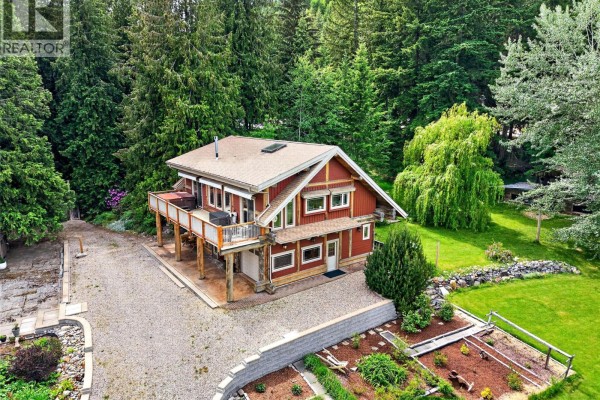 Red cedar-sided house with large wooden deck and multiple windows nestled amongst tall green trees. - 2030 Solsqua-sicamous Road, Sicamous