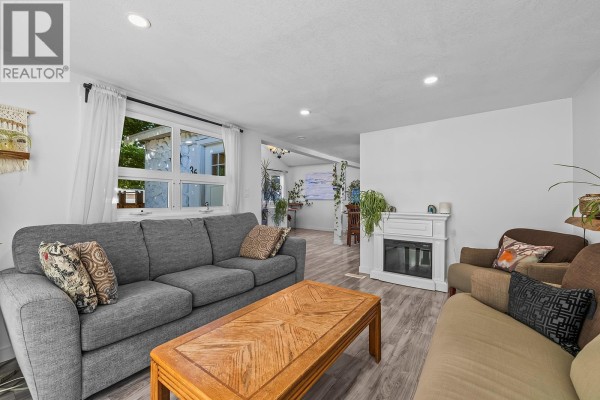 Living room with grey sofa, brown armchair, coffee table, and fireplace with white mantel. - 2035 Boucherie Road Unit# 36, West Kelowna