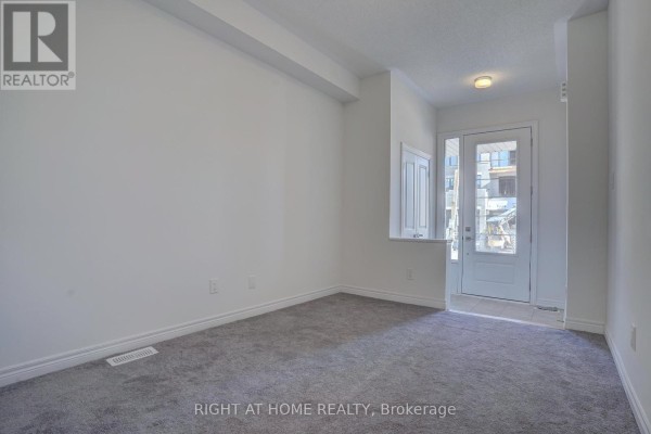 Empty living room with grey carpet, white walls, and a view of the front entryway. - 2038 Cameron Lott Crescent, Oshawa