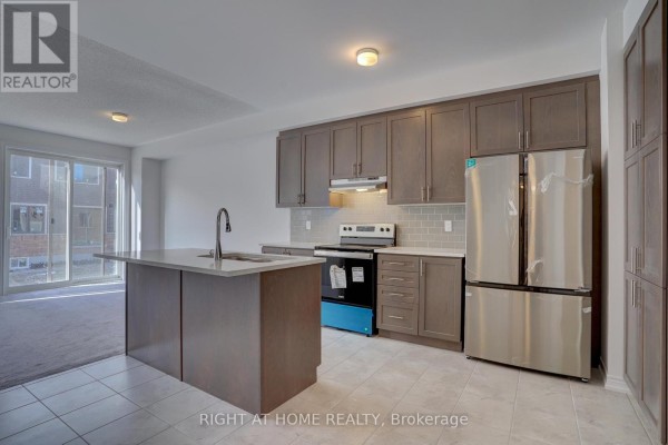 Spacious kitchen with grey cabinets, island, stainless steel refrigerator and stove, and view of a patio door. - 2038 Cameron Lott Crescent, Oshawa