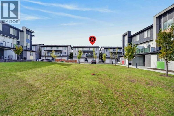 View of the townhouse complex with a large grassy courtyard in the center. - 204, 235 Redstone Walk Ne, Calgary
