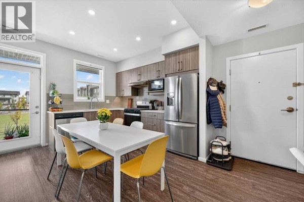 Open concept kitchen and dining area with stainless steel appliances and a white table. - 204, 235 Redstone Walk Ne, Calgary