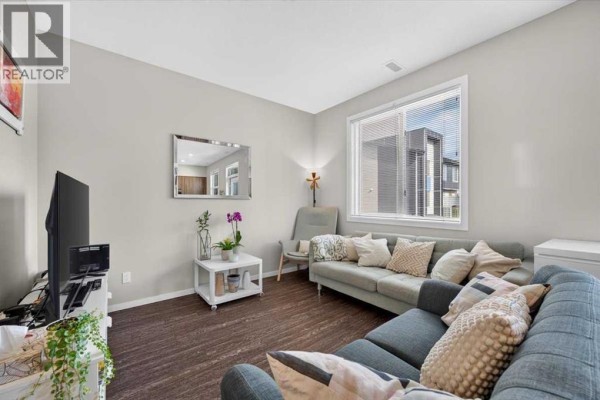 Living room featuring a sectional sofa, television, and a window overlooking the street. - 204, 235 Redstone Walk Ne, Calgary