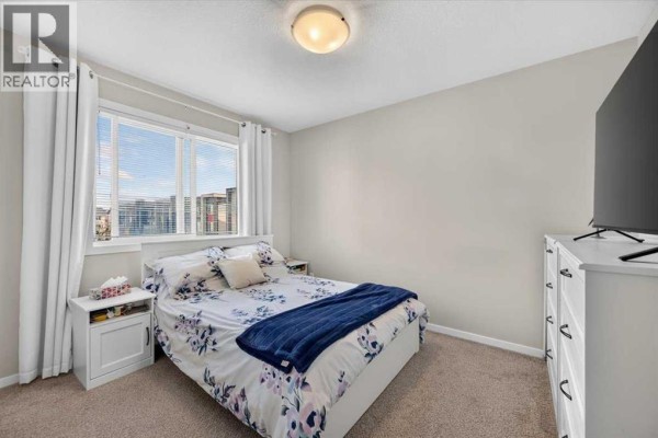 A bedroom with a queen-sized bed, dresser, and a large window with blinds. - 204, 235 Redstone Walk Ne, Calgary
