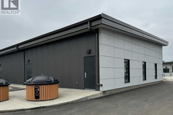 Rear exterior of the commercial building with dark grey ribbed siding, a door, and concrete bins. - 204, 4979 Southlands Drive Se, Medicine Hat