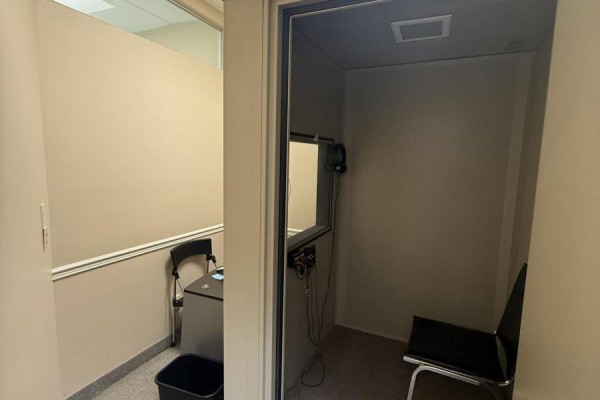 Interior of a small soundproof booth with a chair, headphones, and an adjacent office space. - 204 - 1 Quarry Ridge Road, Barrie
