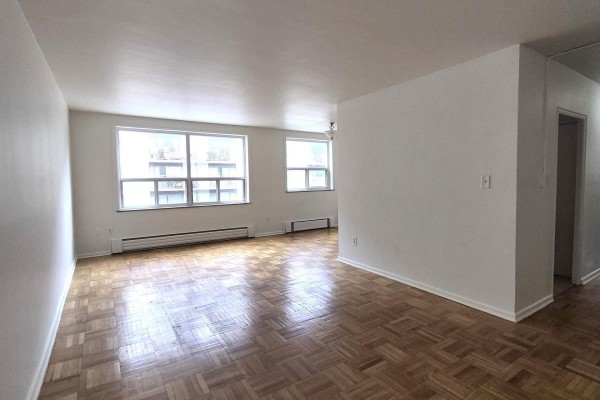 Living room with light grey walls, parquet flooring, two large windows, and a baseboard heater. - 204 - 1751 Victoria Pk Avenue, Toronto