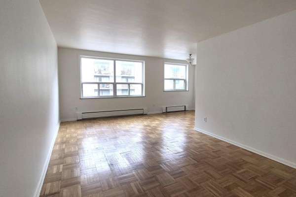 Living room with light grey walls, parquet flooring, two large windows, and a baseboard heater. - 204 - 1751 Victoria Pk Avenue, Toronto