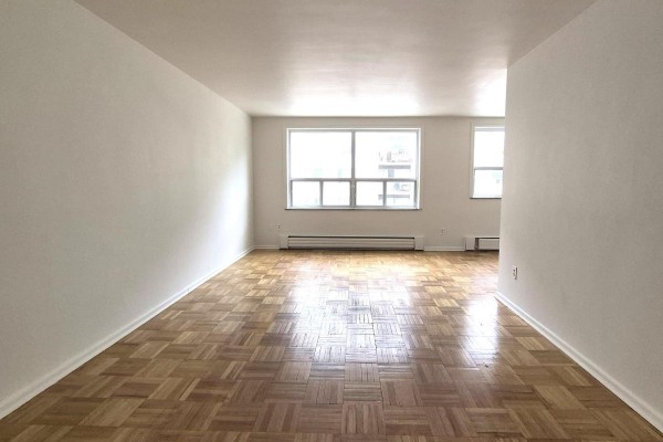 View of a spacious living area with light grey walls, parquet flooring, and two windows showing building views. - 204 - 1751 Victoria Pk Avenue, Toronto