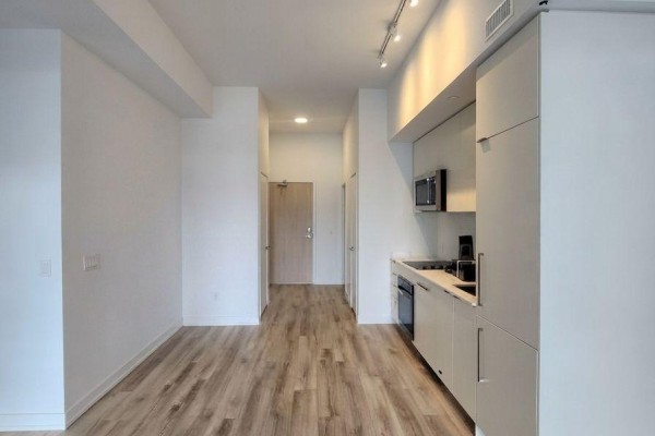 Interior view of a kitchen and hallway with light wood flooring and white walls. - 204 - 181 Sheppard Avenue E, Toronto