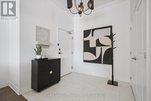 Apartment entryway with a black cabinet, modern art, and white tile flooring. - 204 - 1880 Gordon Street E, Guelph