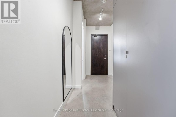 Hallway with white walls, polished concrete floors, and a dark wood door. - 204 - 19 Brant Street, Toronto