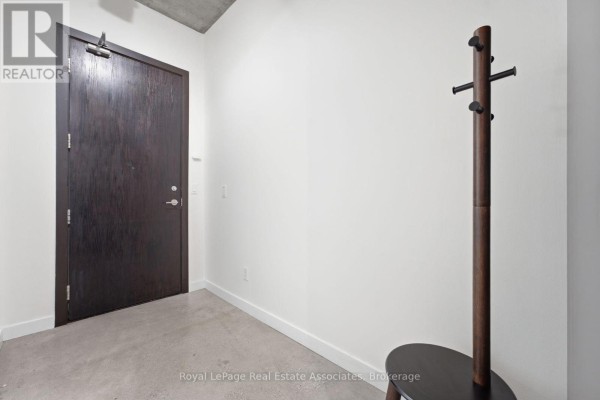 Entrance hallway with a dark wood door, coat rack, and polished concrete floor. - 204 - 19 Brant Street, Toronto