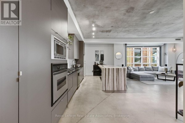 Modern kitchen with grey cabinets, stainless steel appliances, and open living space. - 204 - 19 Brant Street, Toronto
