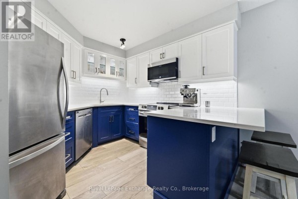 Corner kitchen with white quartz countertops, blue and white cabinets, stainless steel appliances, and subway tile backsplash. - 204 - 200 Harbour Street, Kincardine