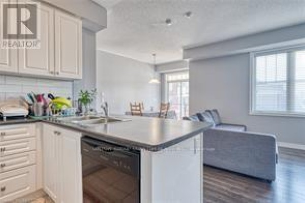 Kitchen island with stainless steel sink overlooking a living and dining area. - 204 - 272 Georgian Drive, Oakville