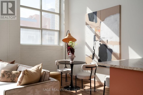 Open concept living space showing a dining table, chairs, and a coral-colored kitchen. - 204 - 284 St Helens Avenue, Toronto