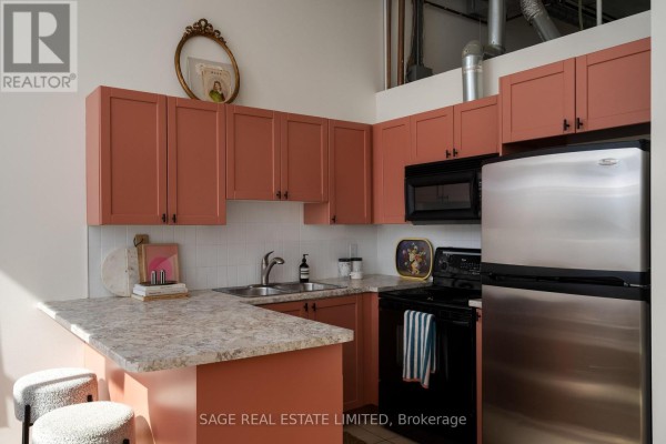 Coral-colored kitchen cabinets with granite countertops, sink, stove, and stainless steel refrigerator. - 204 - 284 St Helens Avenue, Toronto