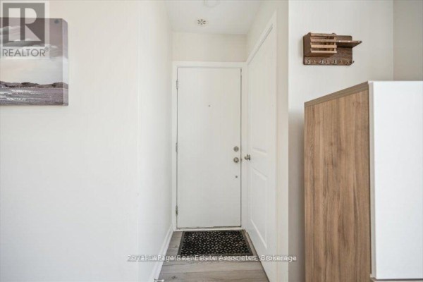 Interior entryway with white door, grey floor mat, and wooden organizer. - 204 - 3058 Sixth Line, Oakville