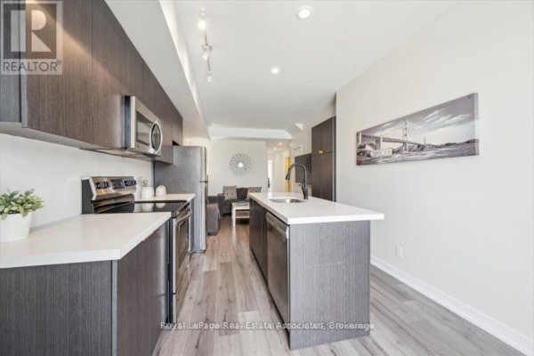 Kitchen with dark wood cabinets, stainless steel appliances and a breakfast bar. - 204 - 3058 Sixth Line, Oakville