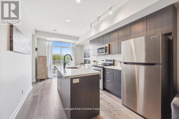 View of the kitchen and living room, including a stainless steel refrigerator. - 204 - 3058 Sixth Line, Oakville