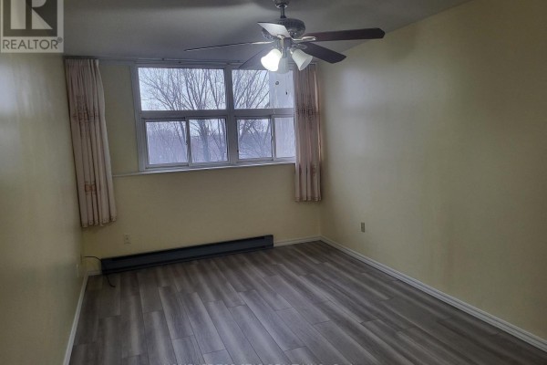Bedroom with yellow walls, grey laminate flooring, a ceiling fan, and a large window. - 204 - 3765 Sheppard Avenue, Toronto