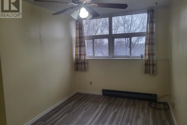 A bedroom with light yellow walls, wood-look laminate flooring, a ceiling fan, and a large window. - 204 - 3765 Sheppard Avenue, Toronto