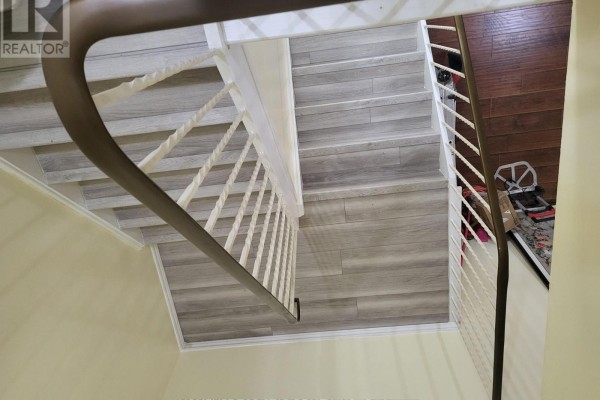 View looking down a white staircase with wood-look laminate treads and a dark wood floor hallway. - 204 - 3765 Sheppard Avenue, Toronto
