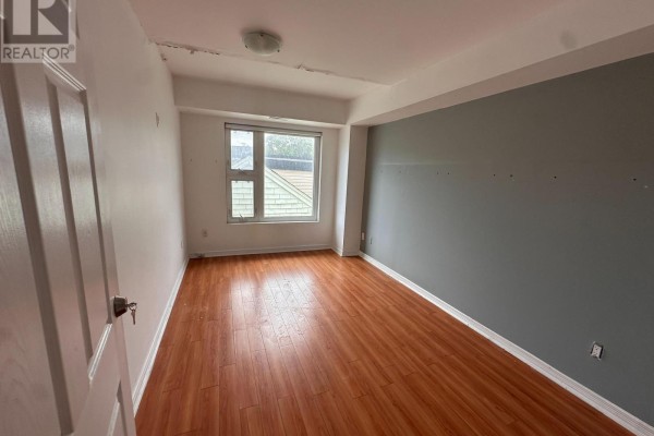 View of second empty bedroom with wood laminate flooring and grey accent wall. - 204 - 38 Kensington Place, Toronto