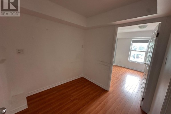 Small empty room with wood laminate flooring, white walls, and doorway to bedroom. - 204 - 38 Kensington Place, Toronto