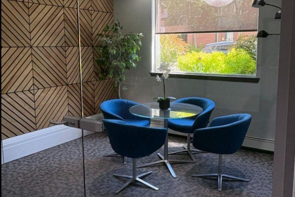 Small meeting area with a glass table, blue chairs, and wood paneled wall. - 204 - 429 Somerset Street W, Ottawa