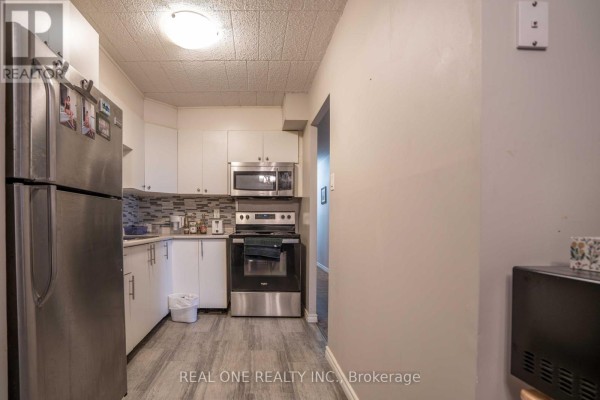 View of a small kitchen with stainless steel appliances and light grey floor. - 204 - 6 Walton Avenue, Kitchener