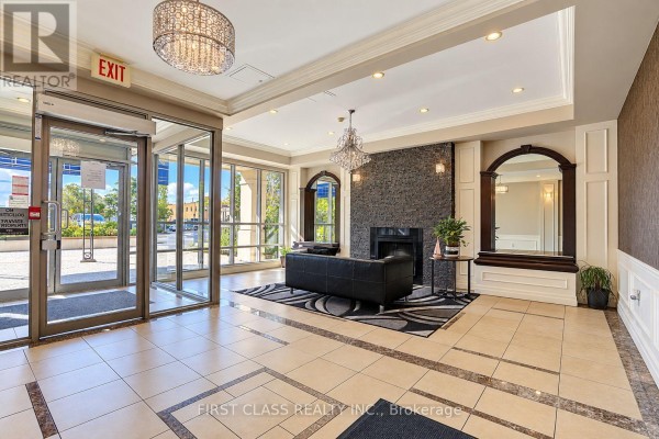 Building lobby with a fireplace, black sofa, patterned rug, and tiled floor. - 204 - 777 Steeles Avenue W, Toronto