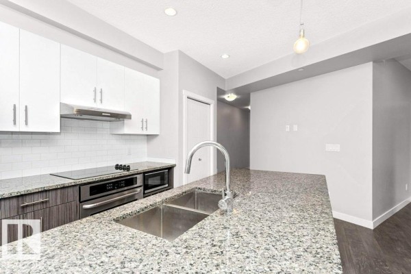 Compact laundry room with stacked white washer and dryer, grey tiled floor, and a black wall-mounted shoe rack. - #204 10126 144 St Nw, Edmonton