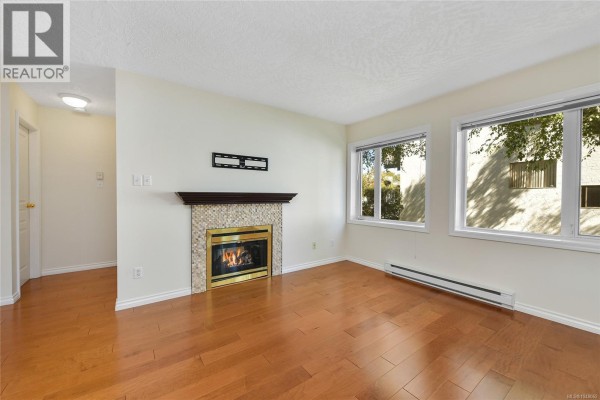 Living room with fireplace, windows, and wood floors looking towards hallway. - 204 1037 Richardson St, Victoria