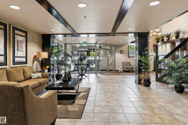 Building lobby with a sofa, coffee table, tiled floor, potted plants, and entrance doors. - #204 121 Festival Wy, Sherwood Park