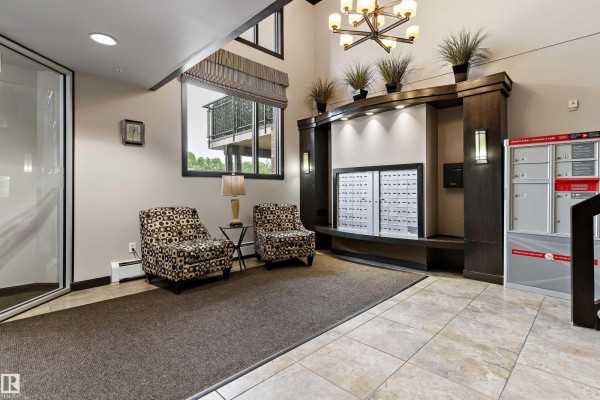 Building lobby with two patterned armchairs, a small table, mailboxes, and a dark wood feature wall. - #204 121 Festival Wy, Sherwood Park