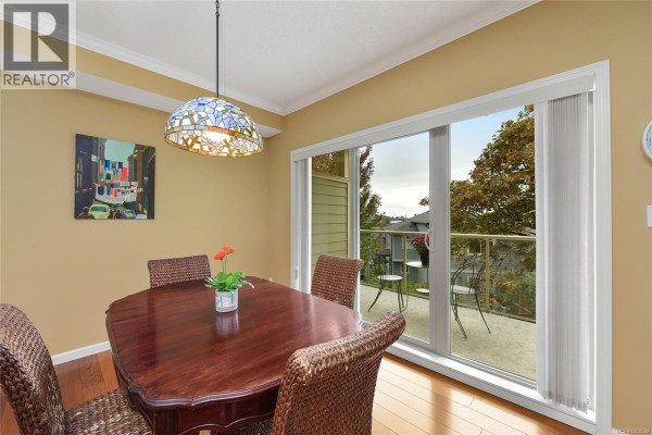 Dining room with a table, chairs, and patio doors overlooking trees and apartments. - 204 125 Aldersmith Pl, View Royal