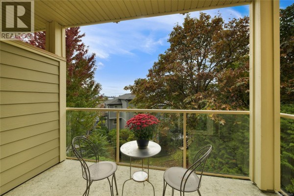 Balcony with glass railings, metal chairs, a small table, and surrounding trees. - 204 125 Aldersmith Pl, View Royal