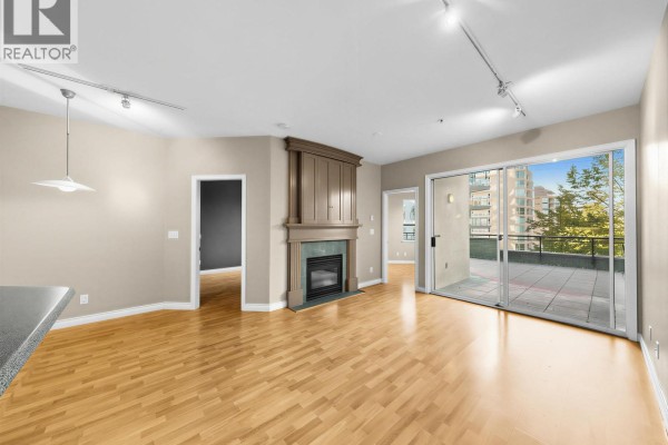 Living room with hardwood floors, gas fireplace, and sliding glass doors to a patio. - 204 131 W 3rd Street, North Vancouver
