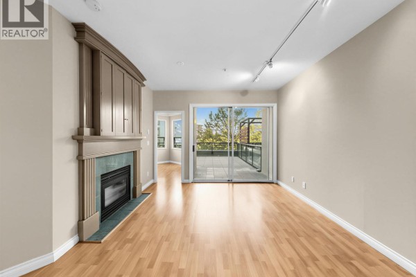 Living room featuring hardwood floors, fireplace, and balcony access with a tree-lined view. - 204 131 W 3rd Street, North Vancouver