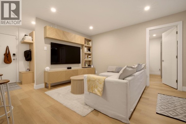 Living room featuring a large sectional sofa, entertainment unit with television, and access to a bedroom. - 204 1345 Comox Street, Vancouver
