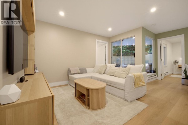 Living room with white sectional sofa, wooden coffee table, entertainment unit, and patio doors. - 204 1345 Comox Street, Vancouver