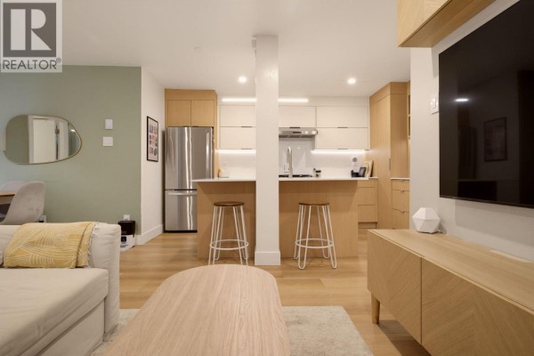 Kitchen with stainless steel refrigerator, island with stools, and light wood cabinetry. - 204 1345 Comox Street, Vancouver