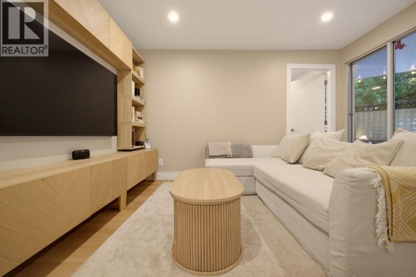 Living room with white sectional sofa, textured rug, and patio doors leading outdoors. - 204 1345 Comox Street, Vancouver