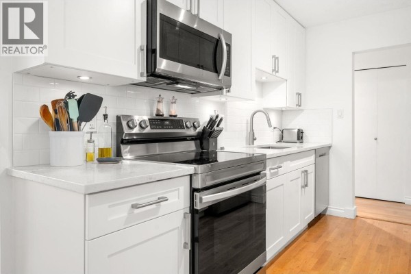 Close-up of white kitchen cabinets, stainless steel stove, microwave, and subway tile backsplash. - 204 150 E 5th Street, North Vancouver