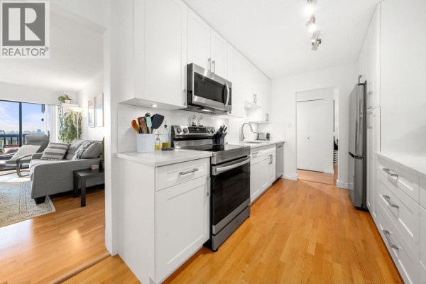 View from the kitchen into a living room with a sofa and large windows. - 204 150 E 5th Street, North Vancouver