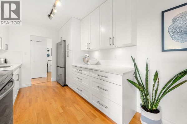 White kitchen cabinets with stainless steel appliances, marble countertops, and wood floors with a plant. - 204 150 E 5th Street, North Vancouver